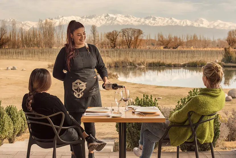 Mujer sirviendo vino a una pareja frente al lago y finca.